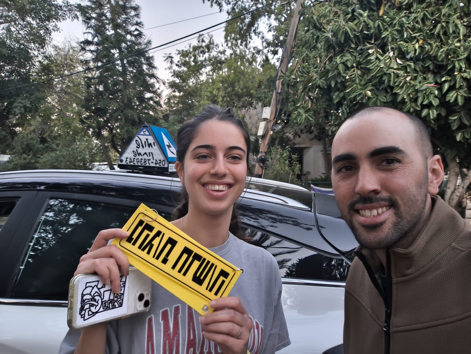 תלמיד עם שלומי שמחון, מורה נהיגה, מחזיק שלט "נהג חדש" לאחר המבחן – תמונה 34