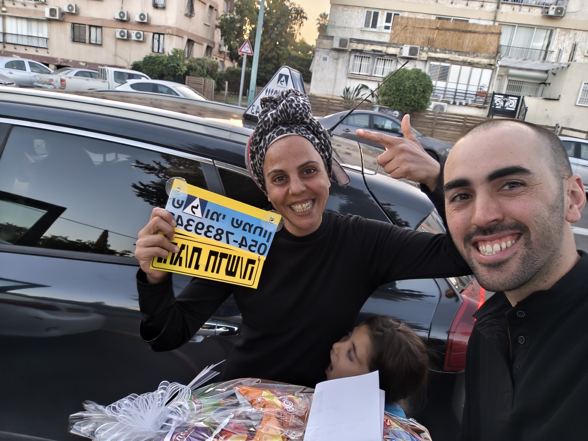 תלמידים עם שלומי שמחון, מורה נהיגה, מחזיקים שלט של בית הספר ביום קבלת הרישיון