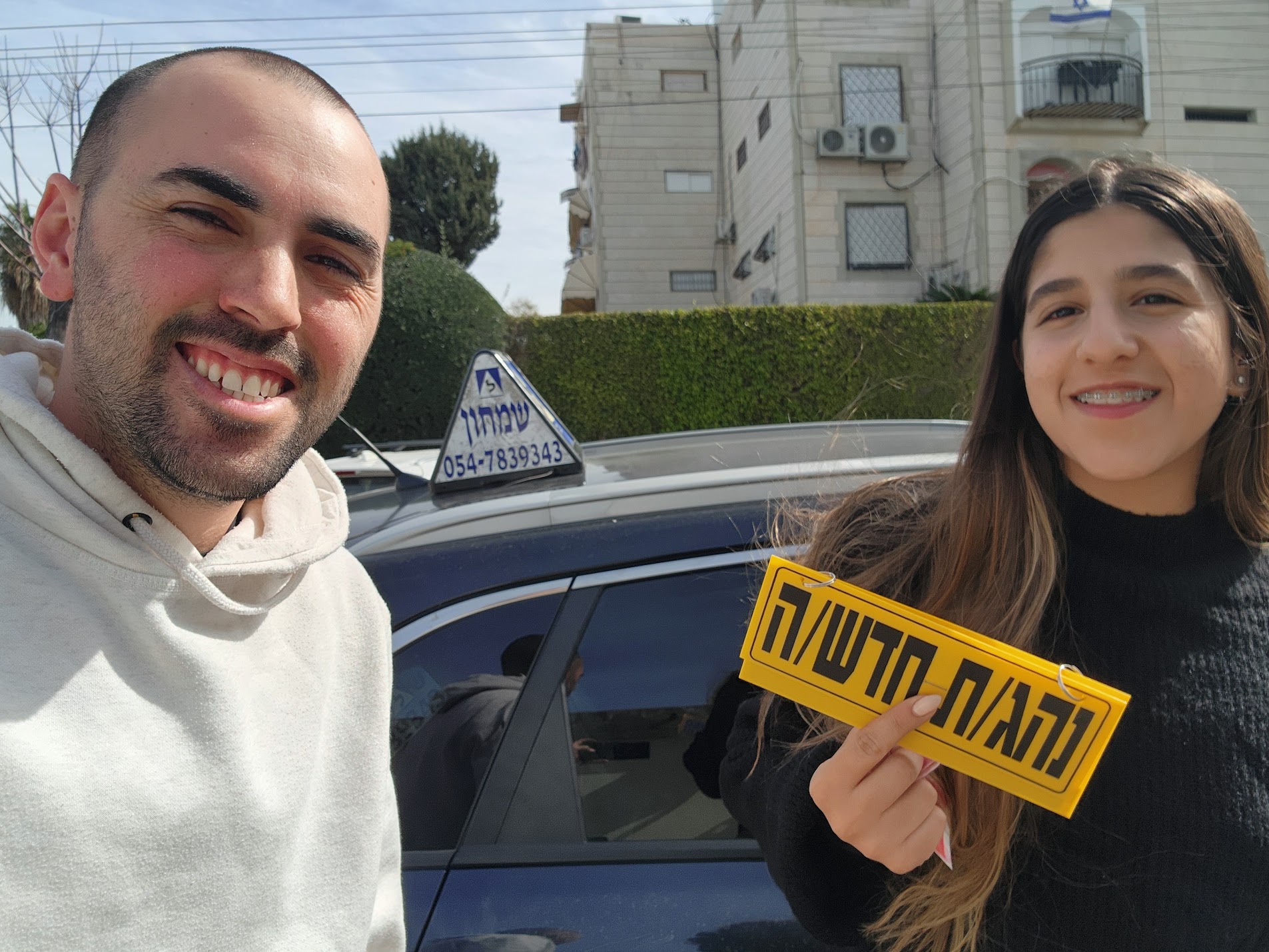 תלמידים עם שלומי שמחון, מורה נהיגה, מחזיקים שלט של בית הספר ביום קבלת הרישיון