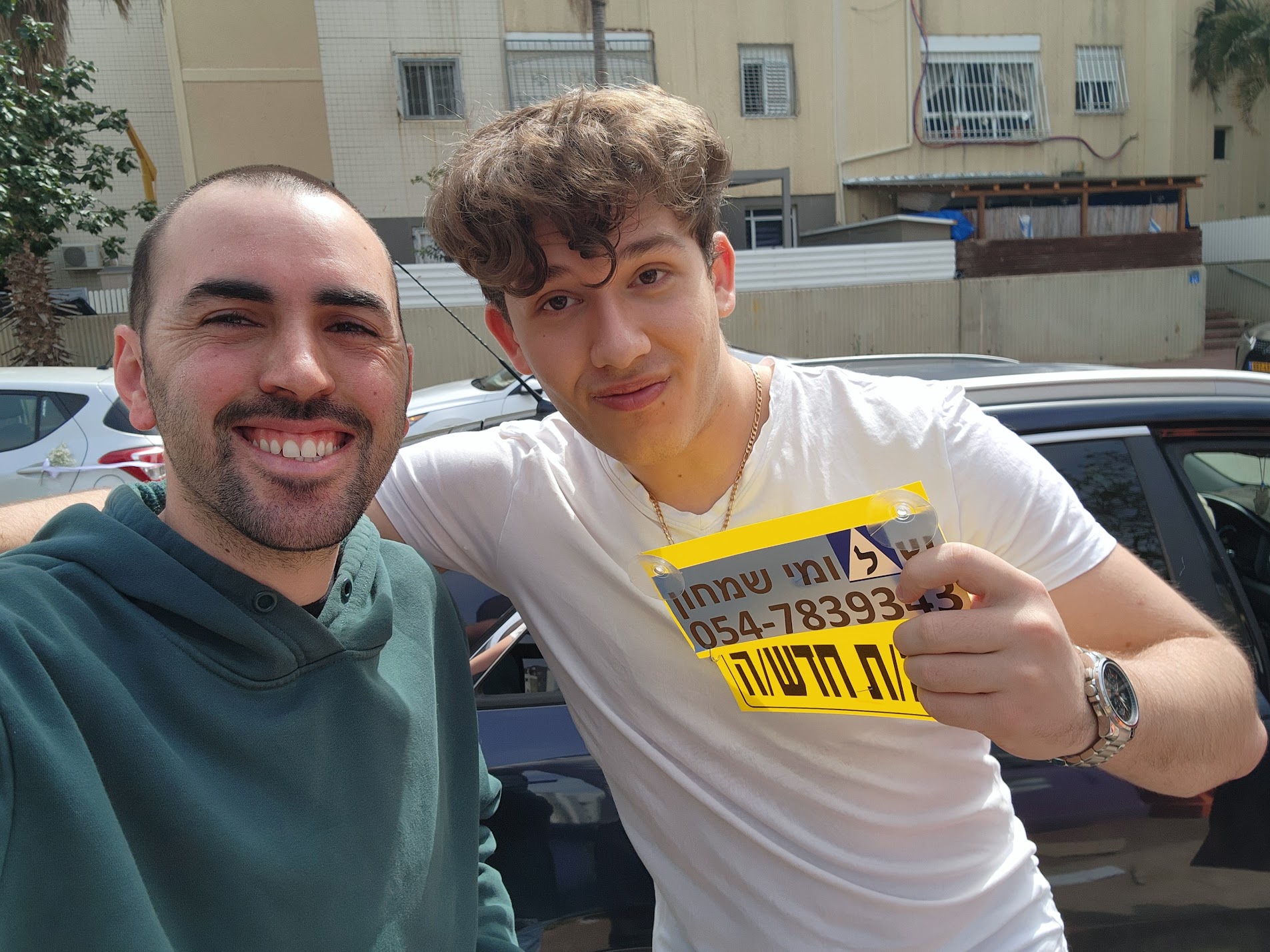 תלמידים עם שלומי שמחון, מורה נהיגה, מחזיקים שלט של בית הספר ביום קבלת הרישיון